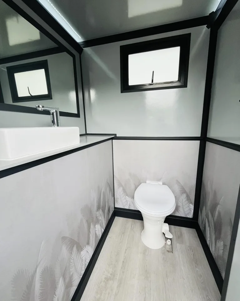 White toilet inside a restroom trailer with windows and dark trim