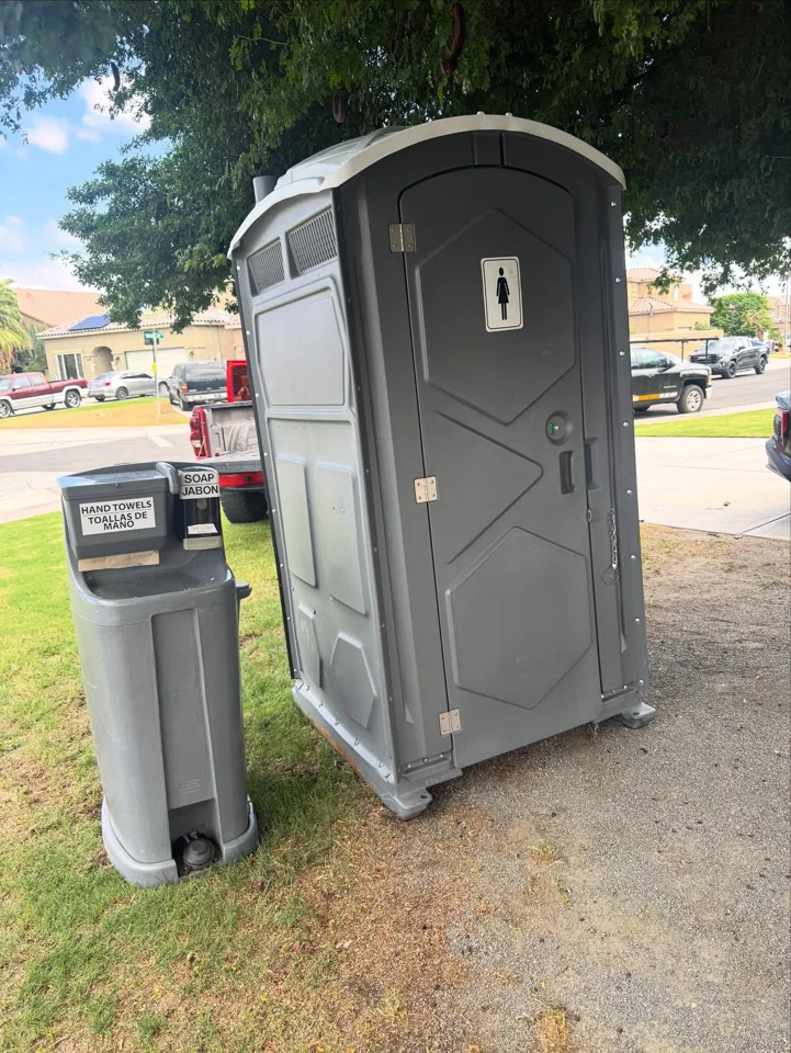 Gray portable toilet beside a separate outdoor handwashing station