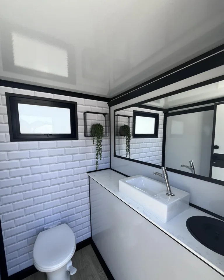 White toilet and dark-countertop vanity inside a restroom trailer