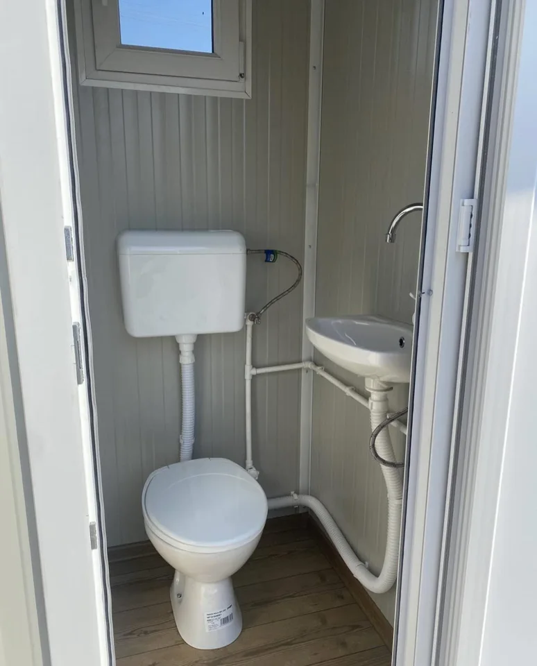 Gray portable restroom interior with a flush toilet and small sink