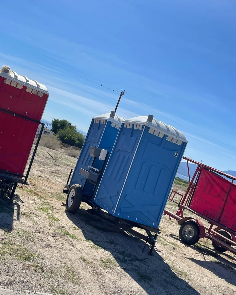Trailer-mounted blue portable toilets beside other equipment