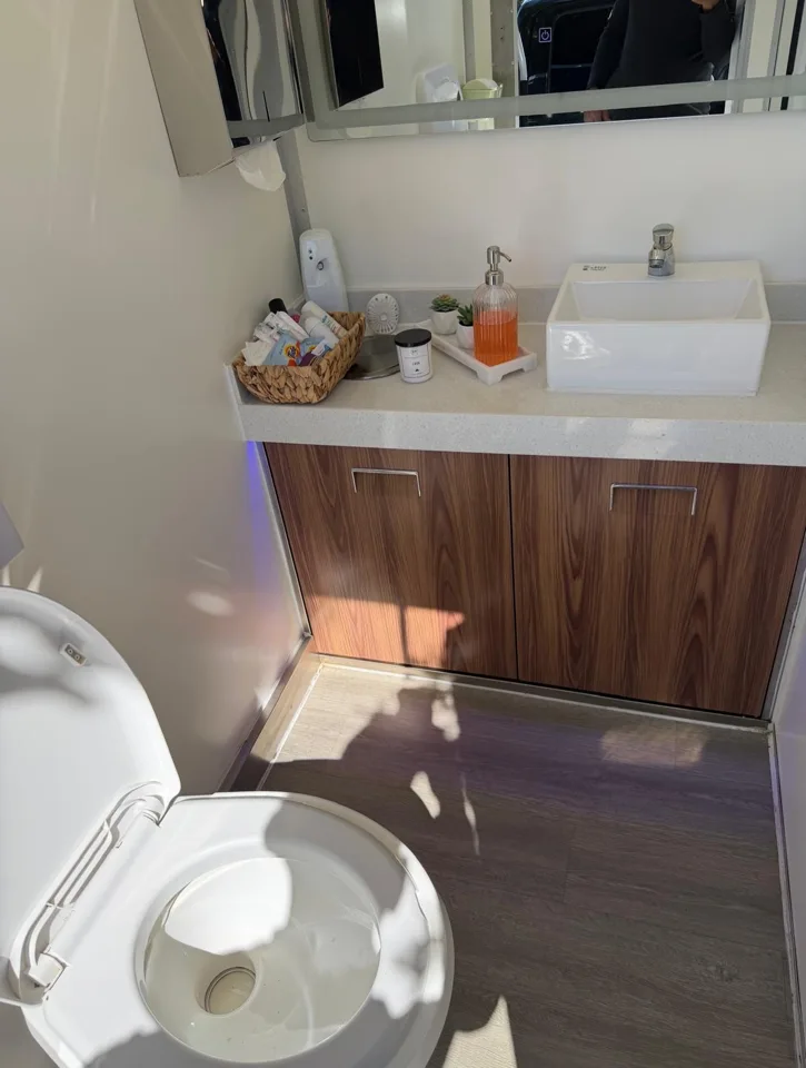 Restroom trailer toilet beside a wood-finish sink vanity