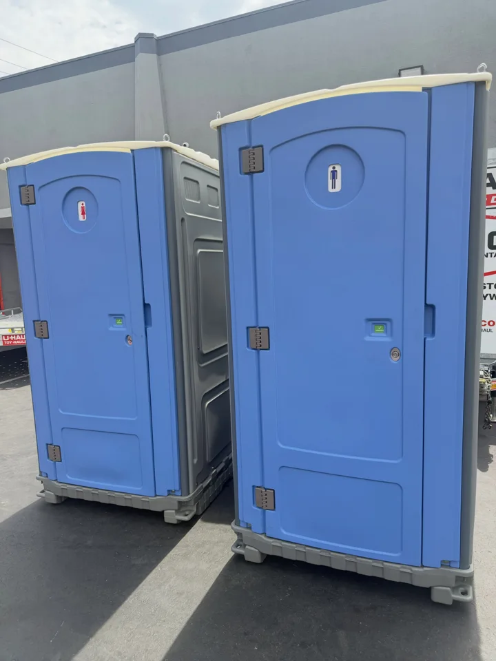 Two purple portable toilets beside a building